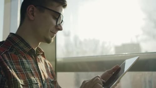 Jovem hipster estiloso usando tablet em um elevador de vidro em um dia ensolarado em Câmera lenta