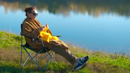 Woman Knitting Outdoors Relaxing By a Lake