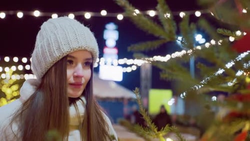 Mulher elegante admirando o pinheiro com luzes festivas no inverno