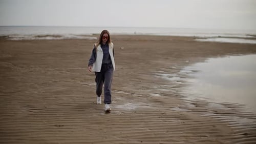 Woman Walking on a Sandy Beach with a Serene Sea Backdrop Creating a Tranquil Scene