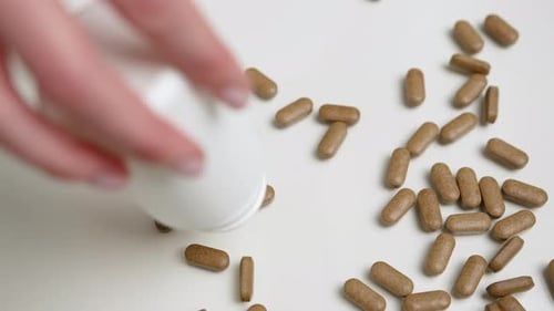 Nahaufnahme natürlicher Kräuterpillen, die aus dem Behälter gegossen werden