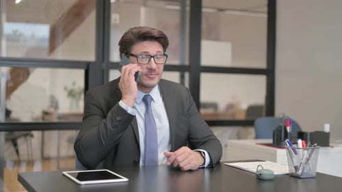 Middle Aged Businessman Talking on phone while Sitting in Office
