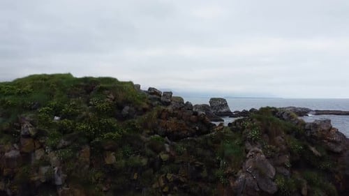 Ascending aerial shot of rocky coastline and shoreline in iceland with clouds at sky