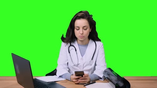 Female Doctor in Uniform Typing on the Smartphone on the Chroma Key