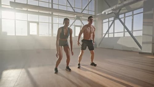 Determined Athletic Young Man and Woman Doing Jumping Jack or Jumping Squats Indoors
