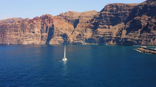 Huge High Mountains and a Lonely White Yacht Drifting in Deep Blue Azure Ocean Waters