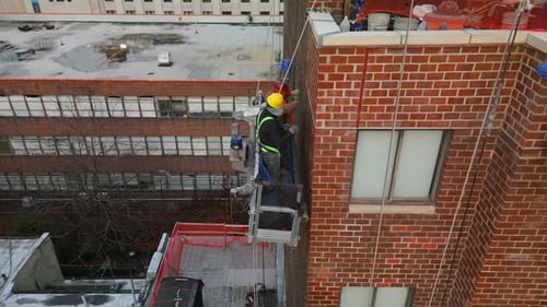Absteigende Luftaufnahmen von zwei Bauarbeitern, die eine Ziegelfassade auf einem Aufzug hoch oben reparieren