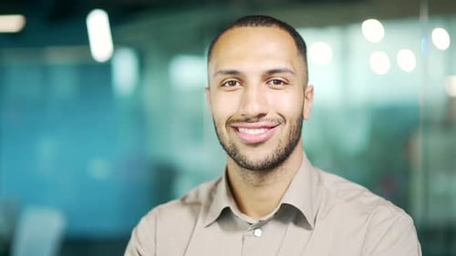 Close up portrait of young adult man in shirt smiling and looking at camera in office. Handsome mixe