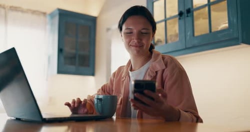Woman Works on Laptop While Looking at Phone