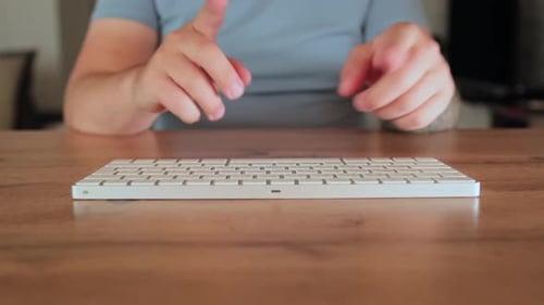 Male tattooed hands typing to music on a modern keyboard close-up.