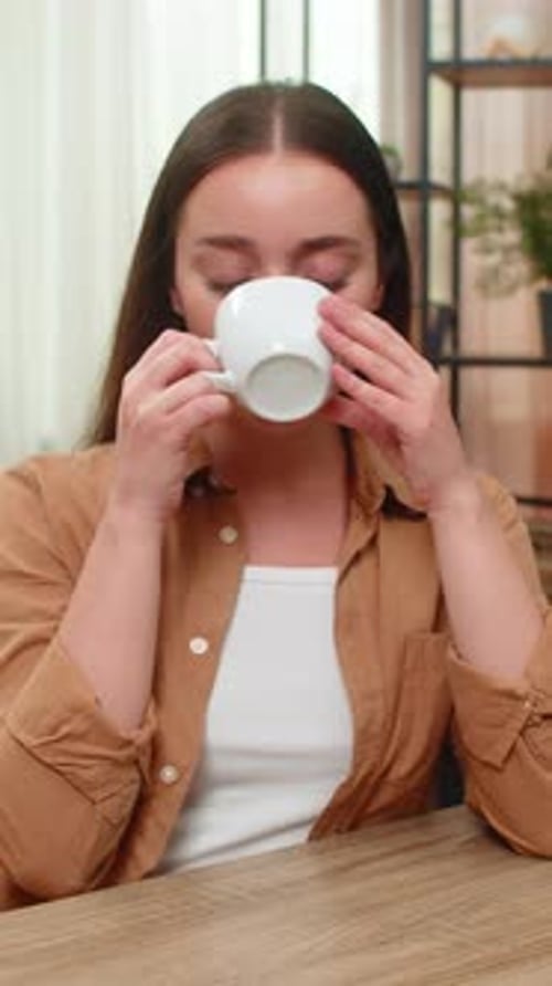 Woman Drinking Coffee and Smiling at Table Indoors