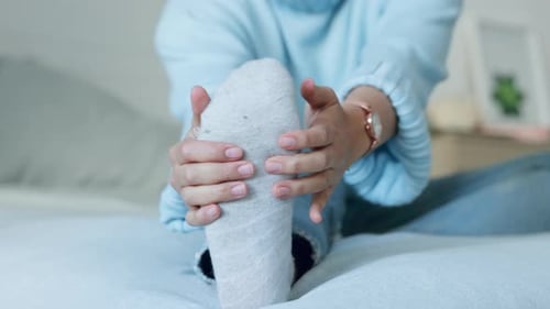 Woman Massages Foot in Bedroom