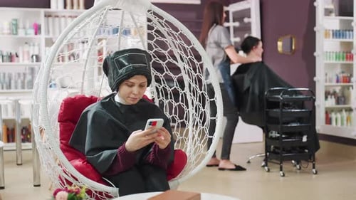 Woman uses phone in salon hair treatment chair