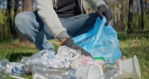 Un hombre recoge basura de una pila que yace en el bosque y la coloca en una bolsa de plástico