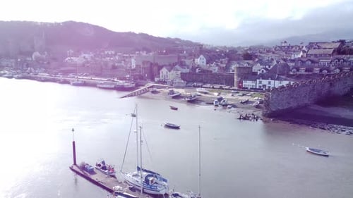 Idyllic Conwy castle and harbour fishing town boats on coastal waterfront aerial fly over boats belo