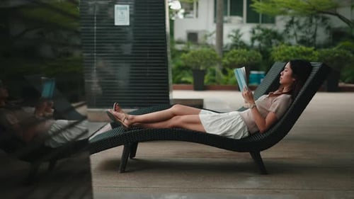 Woman Reading Book on Lounge Chair by Pool