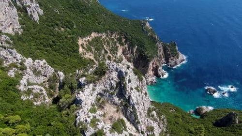 Aerial Drone View of Steep Rocky Cliffs with Green Vegetation Dropping into Turquoise Sea with Seclu