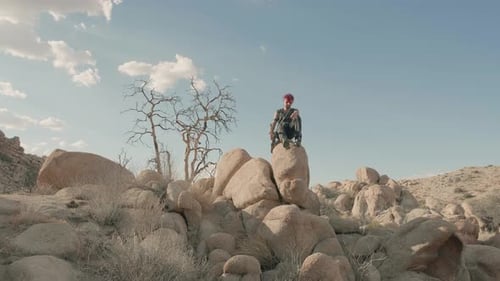Young Punk musician sits atop of large rock amidst desert barren landscape