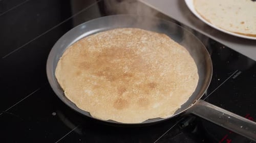Hand flipping pancake with spatula on pan with sizzling sound