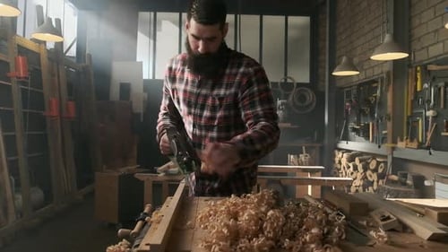 Carpenter planing wood in moody workshop