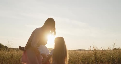 Happy Mother Playing with Her Son Holding Him with Hands in a Golden Field at Sunset