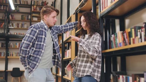 Young Adults Chatting Between Bookshelves in Library