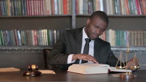 Pensive African Male Lawyer Reading Book in Office
