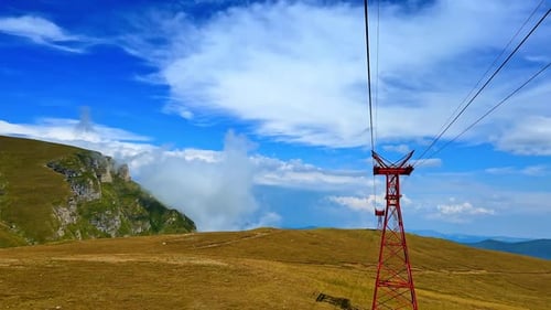 Moving by the cable way by the high mountain. Beautiful azure sky with white clouds at backdrop