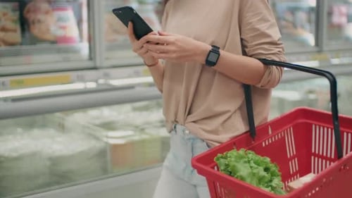 Woman shopping with smartphone in supermarket