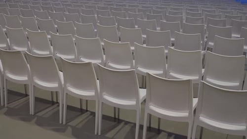 Rows of empty white chairs in an auditorium