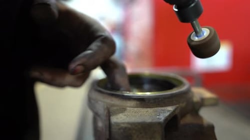 A mechanic with extremely dirty hands is cleaning a housing with a drill to make ready for a new bus