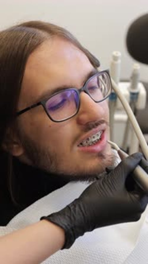 Young Man with Braces Receiving Professional Teeth Cleaning