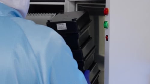 Un technicien ganté en tenue de salle blanche fait fonctionner la chambre de passage en observant les lumières rouges et vertes