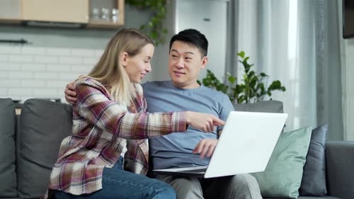 Happy young married couple shopping online choosing a product in online store together on laptop