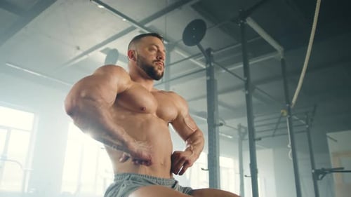 Middleaged Bodybuilder Sits in Gym and Makes Poses Showing His Muscles