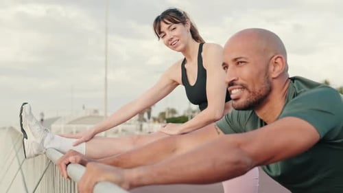 Side view of sportive happy young couple doing legs warms-up and stretching before workout