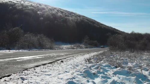 Weite Vollaufnahme einer Autofahrt an einem Wintertag auf trockener Straße und verschneitem Hintergrund
