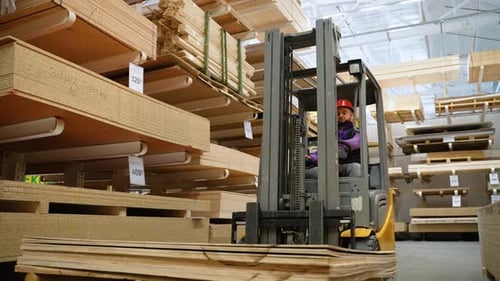 Forklift Driver in Protective Vest Driving Forklift at Lumber Warehouse