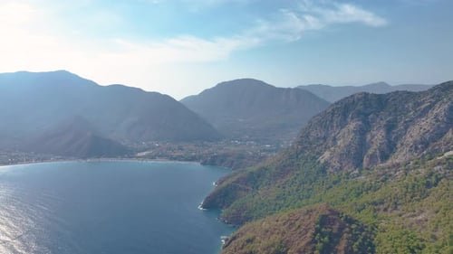 Turquoise Water Meets a Rocky Shore Adorned with Lush Green Trees Sunlight Glistens on the Deep Blue