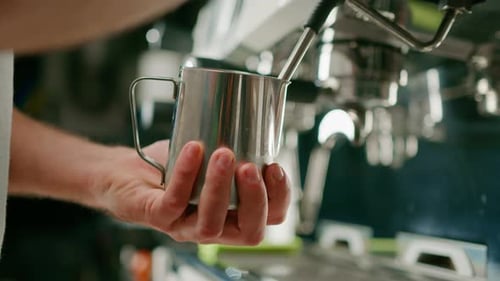 barista uses coffee machine and churns fresh milk to prepare latte or cappuccino in cafe for client