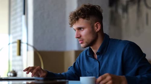 Young Businessman Sitting in Restaurant Texting on Laptop Working Online and Drinking Coffee