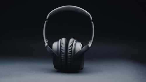 A product shot of black headphones on a black background, standing upright. Camera movement from rig