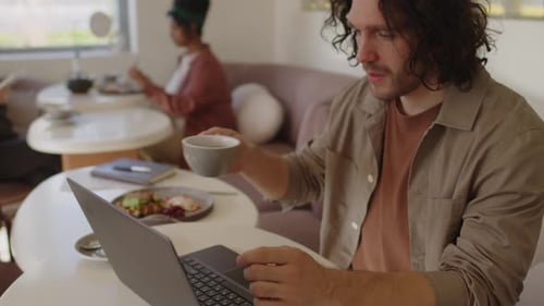 Man Drinking Coffee and Using Laptop In Cafe