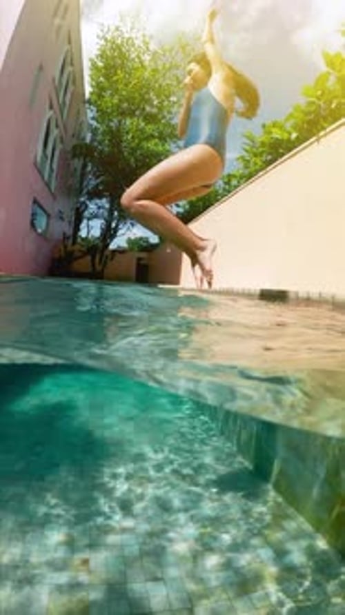 Young Woman Jumping Into Swimming Pool in a Sunny Day
