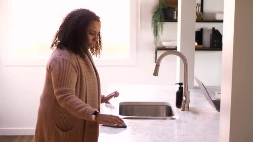 Woman Cleaning Countertop with Sponge in Bright Kitchen