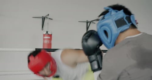 Männliche Boxer mit Helmen und Handschuhen trainieren Sparring im Kampfring des Sportzentrums
