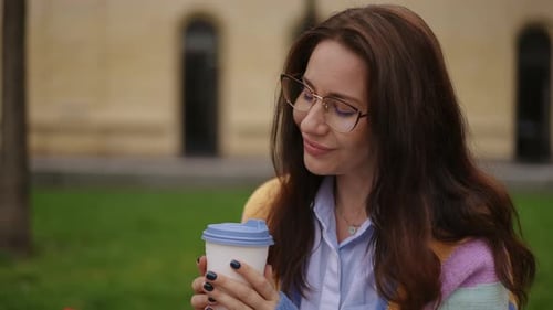 Early in the Morning Sitting on a Bench in the Park a Woman Drinks Coffee From a Paper Cup and