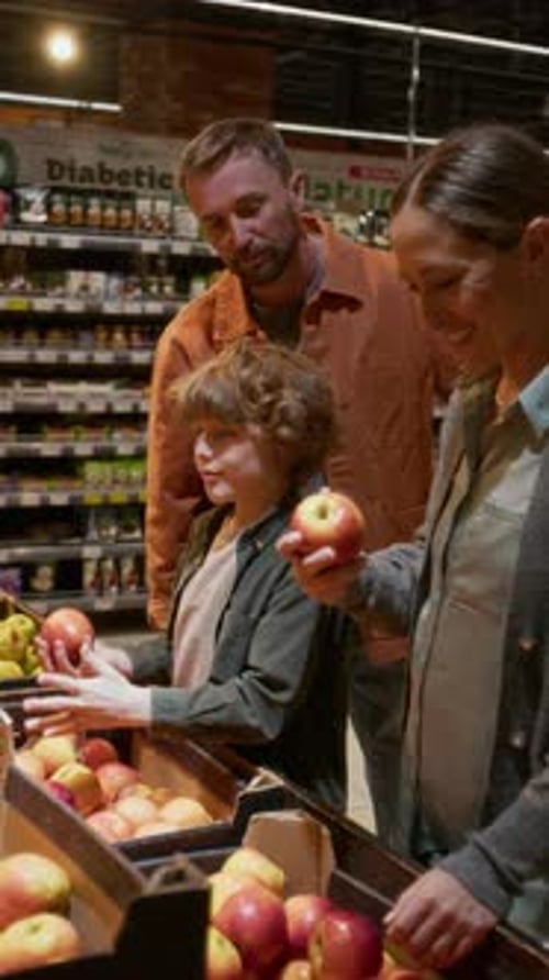 Cheerful Family of Married Couple and Their Son Choosing Apples in Supermarket