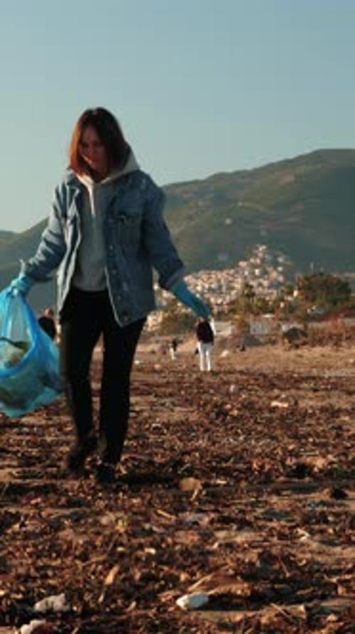 Volunteer in protective gloves cleaning up beach from trash. Vertical video