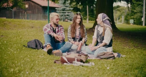 Friends Sitting And Talking On Grass At Park